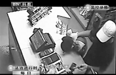 戴帽男子一手掐住加油站營(yíng)業(yè)員，一手持發(fā)令槍指向另一營(yíng)業(yè)員，要求“把錢(qián)給我裝起來(lái)”。