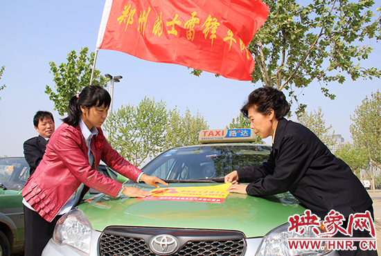　　授旗結(jié)束后，首都的士雷鋒車隊王鳳進隊長（右）與鄭州的的哥的姐在車身上貼上標識。