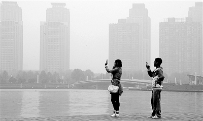 29日中午，鄭東新區(qū)如意湖畔，兩個(gè)年輕人拍攝霧霾中的景色。 鄭州晚報(bào)記者 馬健 圖