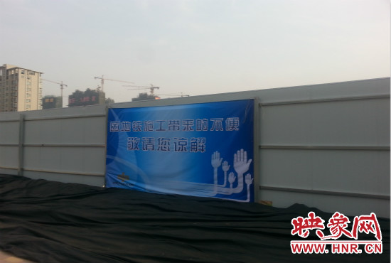道路南側(cè)圍起了白色的圍擋，墻上標(biāo)示著“因地鐵施工帶來的不便敬請您諒解”的提示牌。