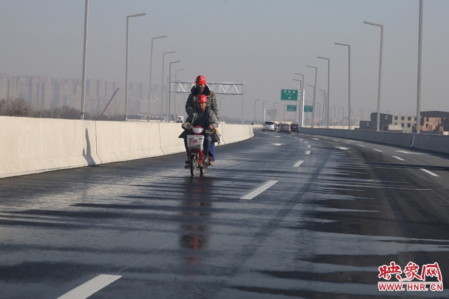 兩名工人騎車經(jīng)過灑水養(yǎng)護路面。