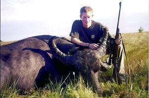 哈里王子手持獵槍，蹲在一頭遭到獵殺的水牛旁邊